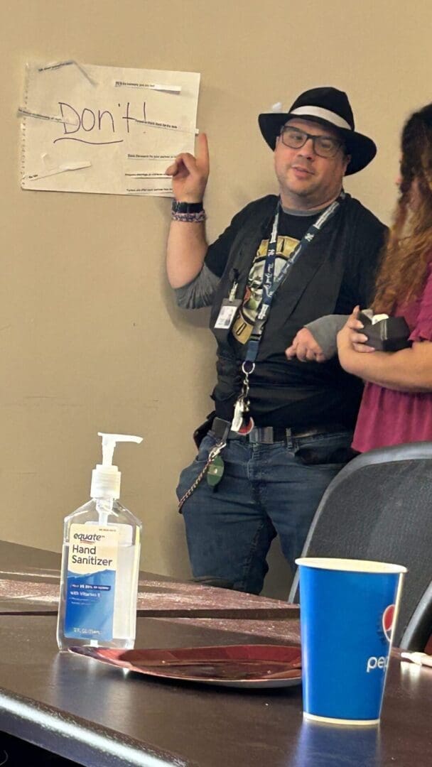 Two people standing near a wall with a sign and sanitizer on a table.