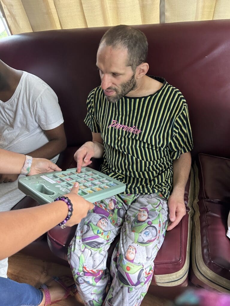 Man sitting on a couch, wearing colorful clothes, while someone shows him money.