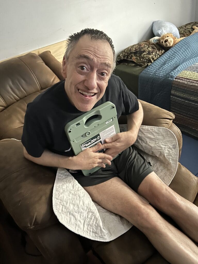 A joyful man holding a green game console while sitting on a couch.