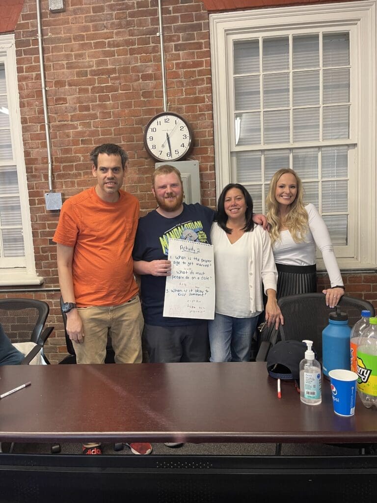 Four people standing indoors holding a poster with cleaning supplies on the table.