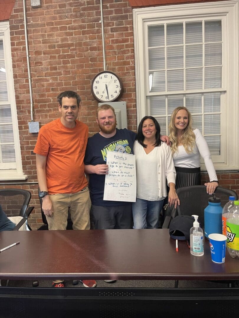 Four people standing indoors holding a poster with cleaning supplies on the table.