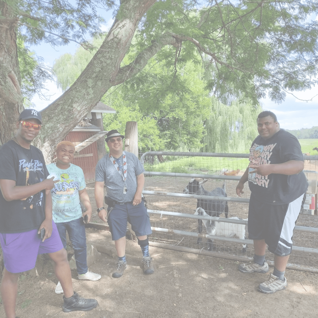 A group of five people posing near a fenced area with trees and a goat.