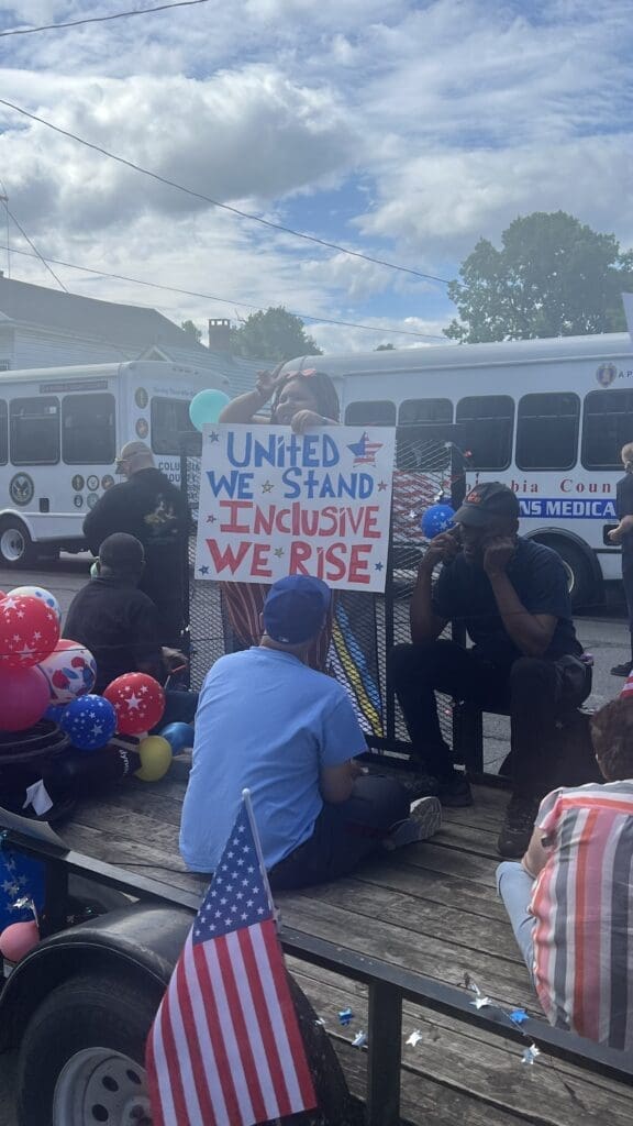 People gather outdoors holding a sign about unity and rising together.