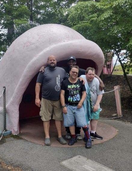 Three people posing in front of a large ear sculpture outdoors.