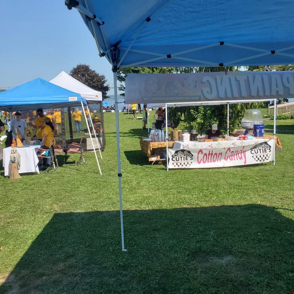 Outdoor market stalls under blue tents on a sunny day.