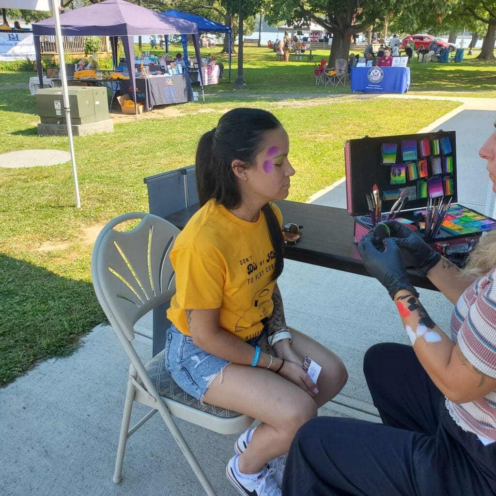 A young woman getting her face painted at an outdoor event.