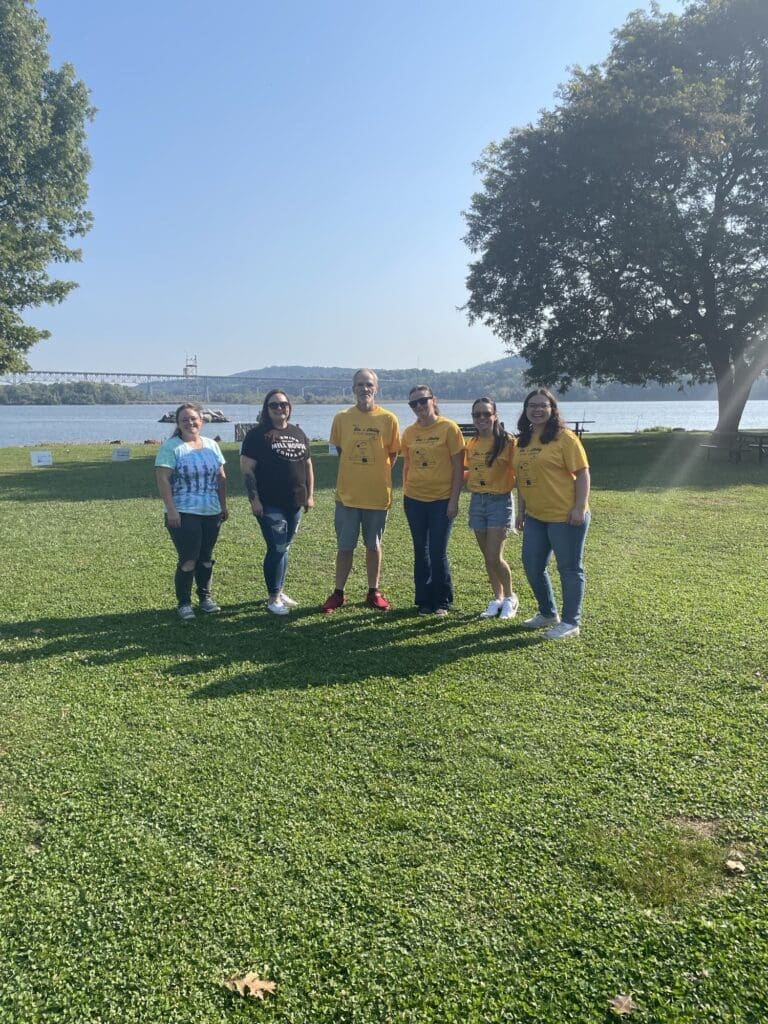 Five people standing on grass near a lake, smiling and posing for a photo.