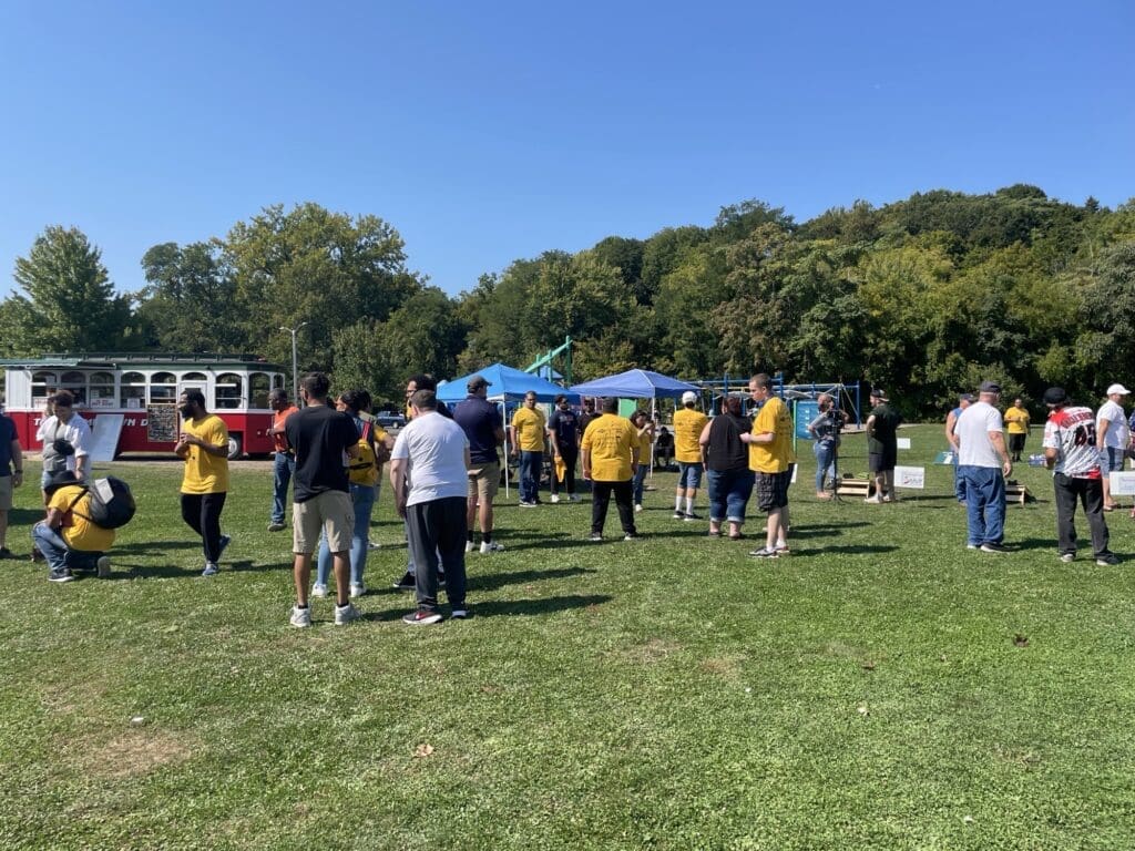 People gathered outdoors near tents and buses on a sunny day.