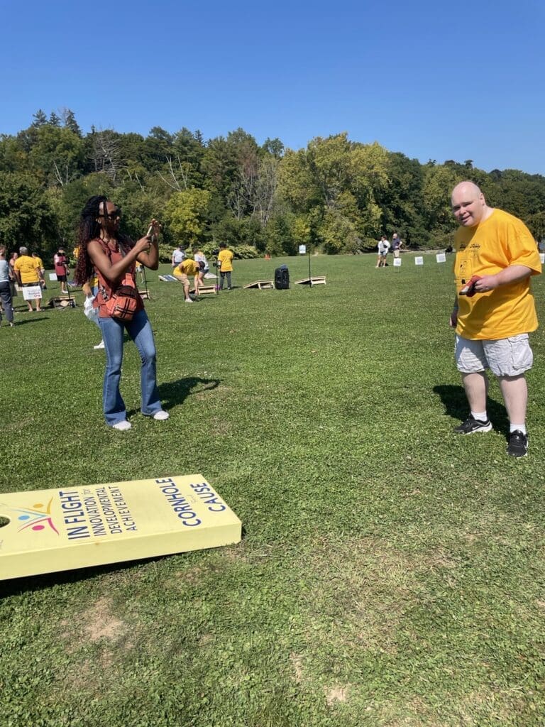 Two people playing cornhole outdoors on a sunny day.
