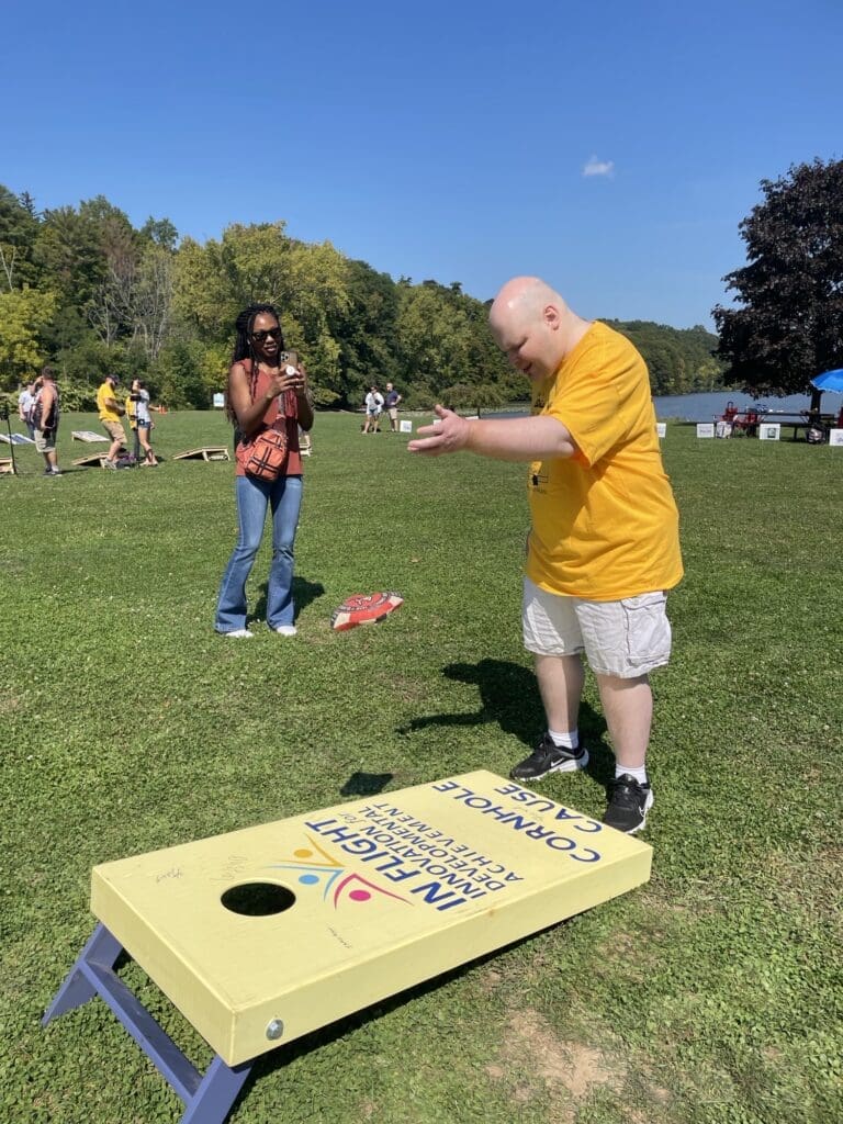 Man in yellow playing cornhole outdoors on a sunny day.