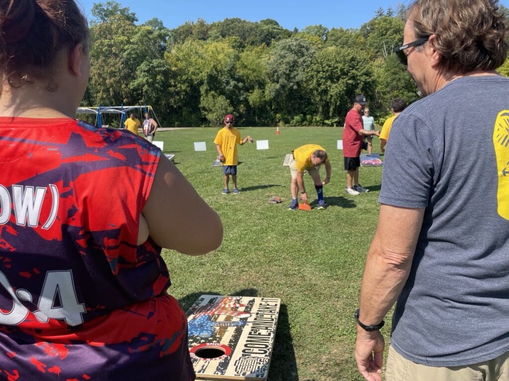 People gathered outdoors around a table and a man setting up a game.