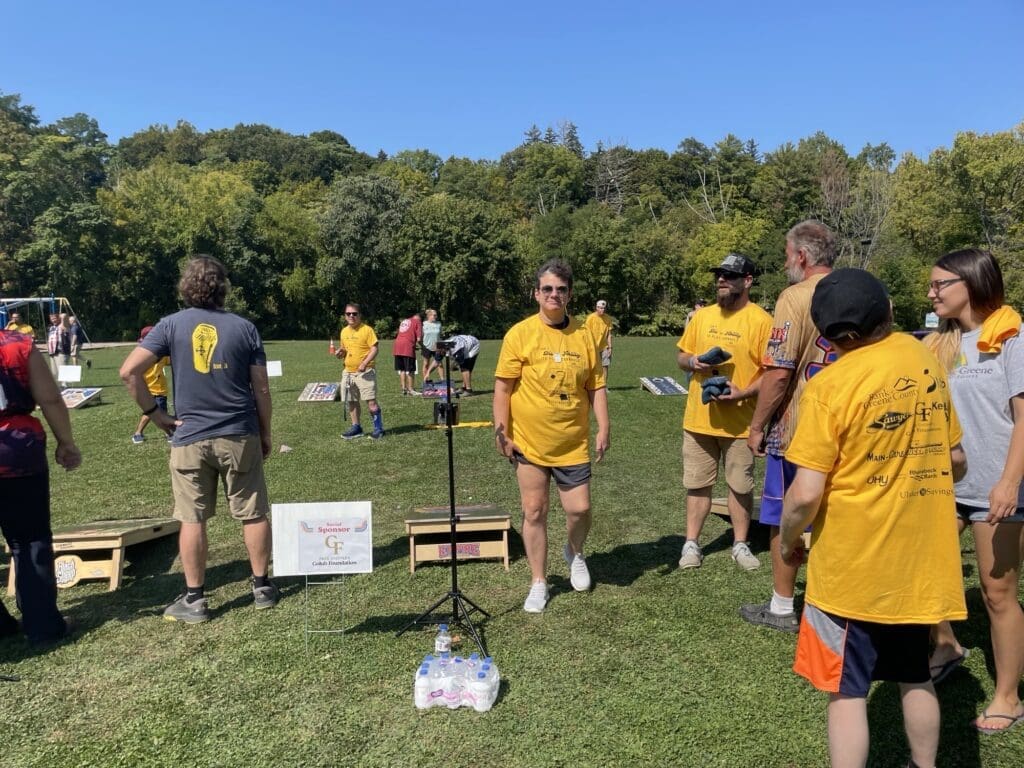 People in yellow shirts playing cornhole outdoors on a sunny day.