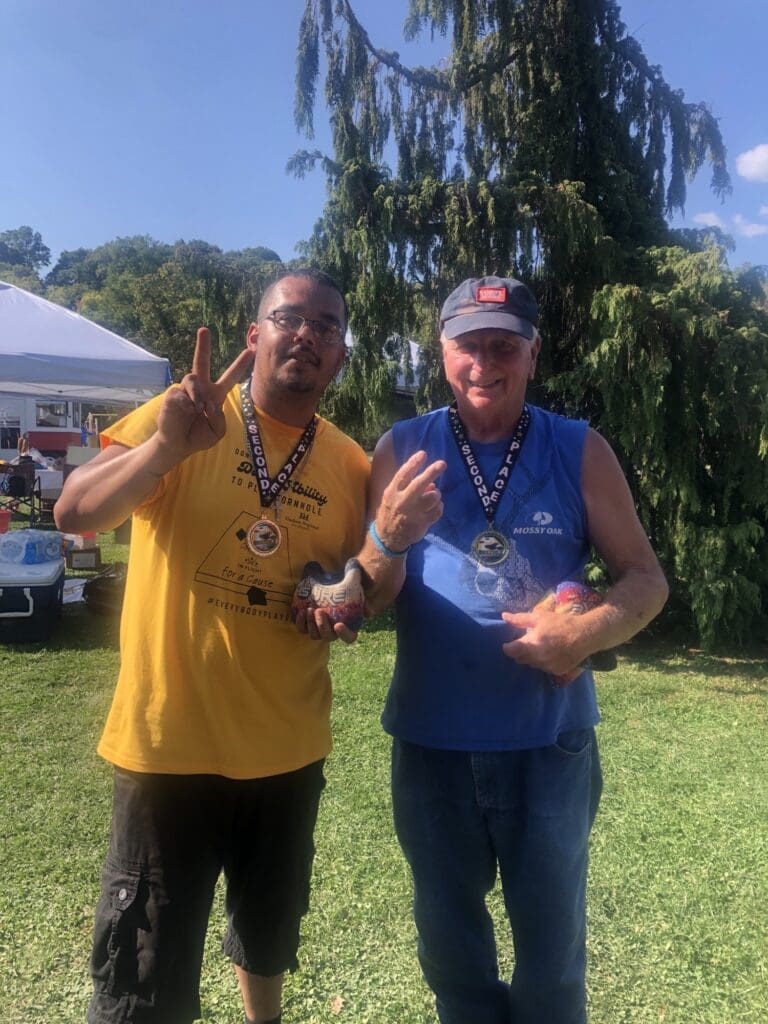 Two men smiling and posing outdoors at a sunny event.