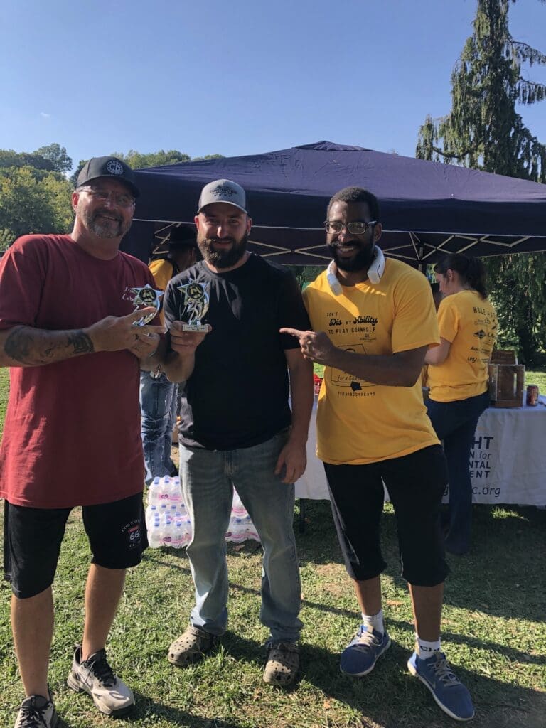 Three men outdoors, one holding a trophy, celebrating together.