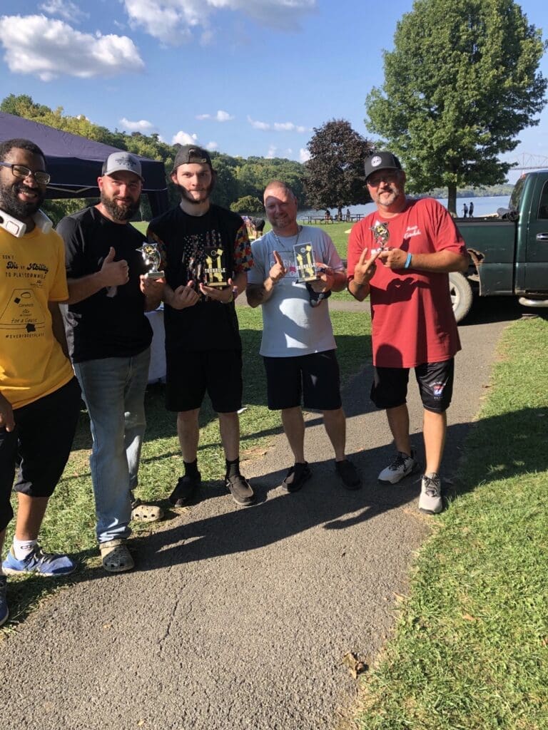 Five men standing together outdoors on a sunny day, smiling and posing for a photo.