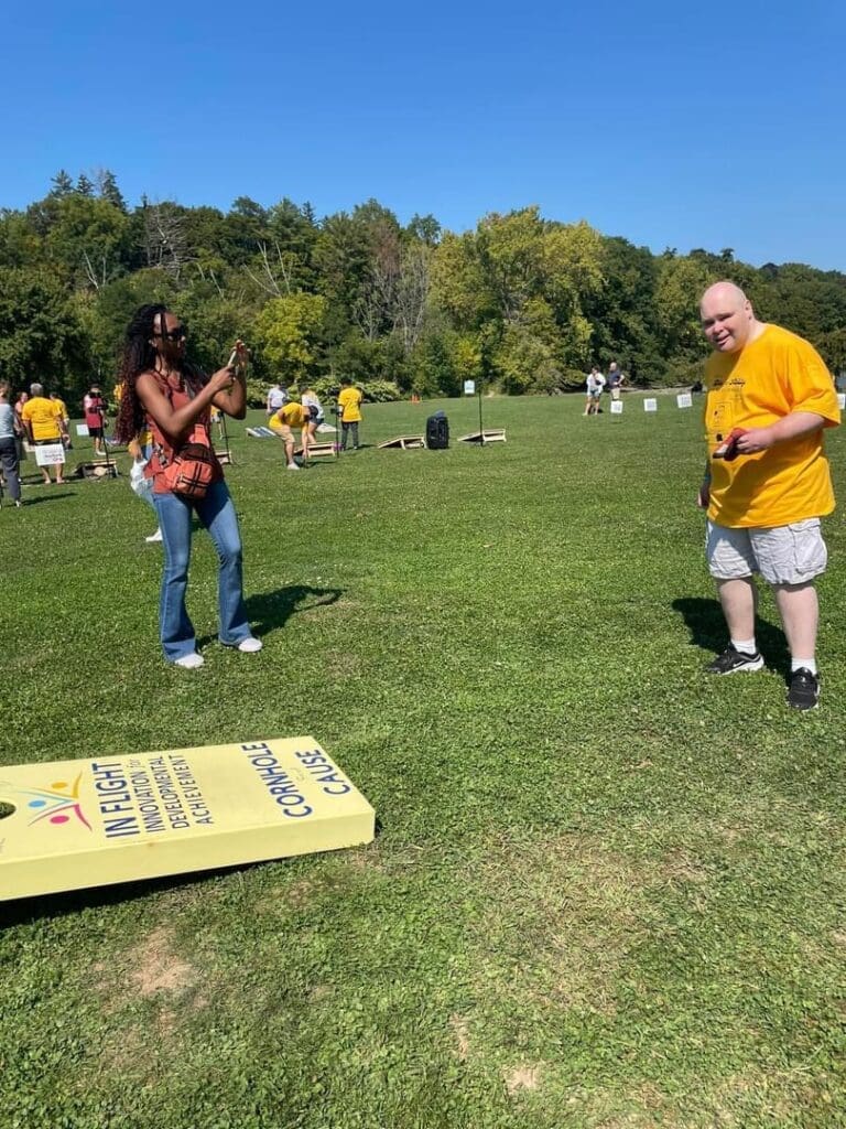 Two people playing cornhole outdoors on a sunny day.