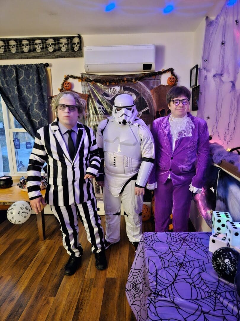 Three people in Halloween costumes standing indoors with decorations.