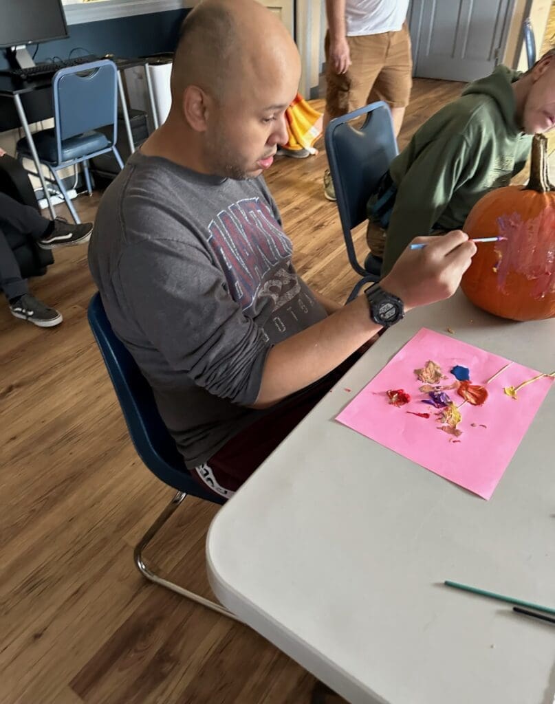 Man painting small art pieces on pink paper at a table.