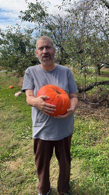 Man holding a large orange pumpkin outdoors.
