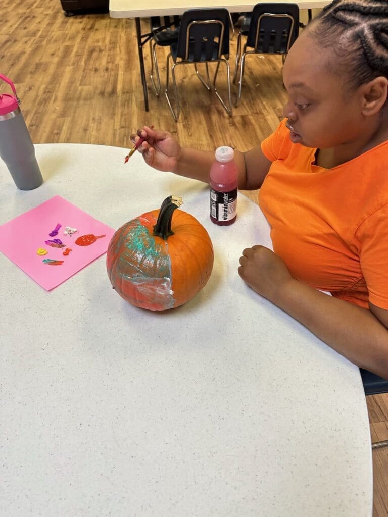 Child painting a pumpkin orange and silver at a table.