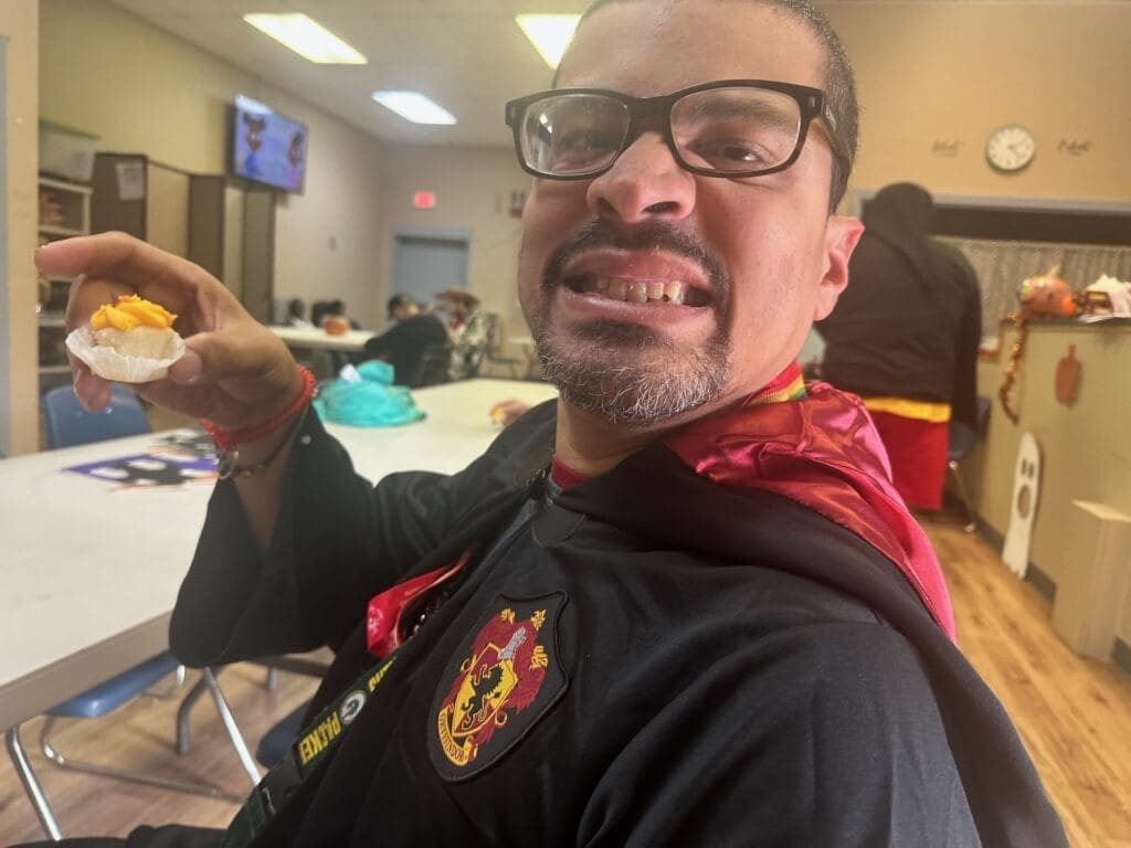 Person smiling indoors wearing glasses and a Hogwarts-themed sweater.