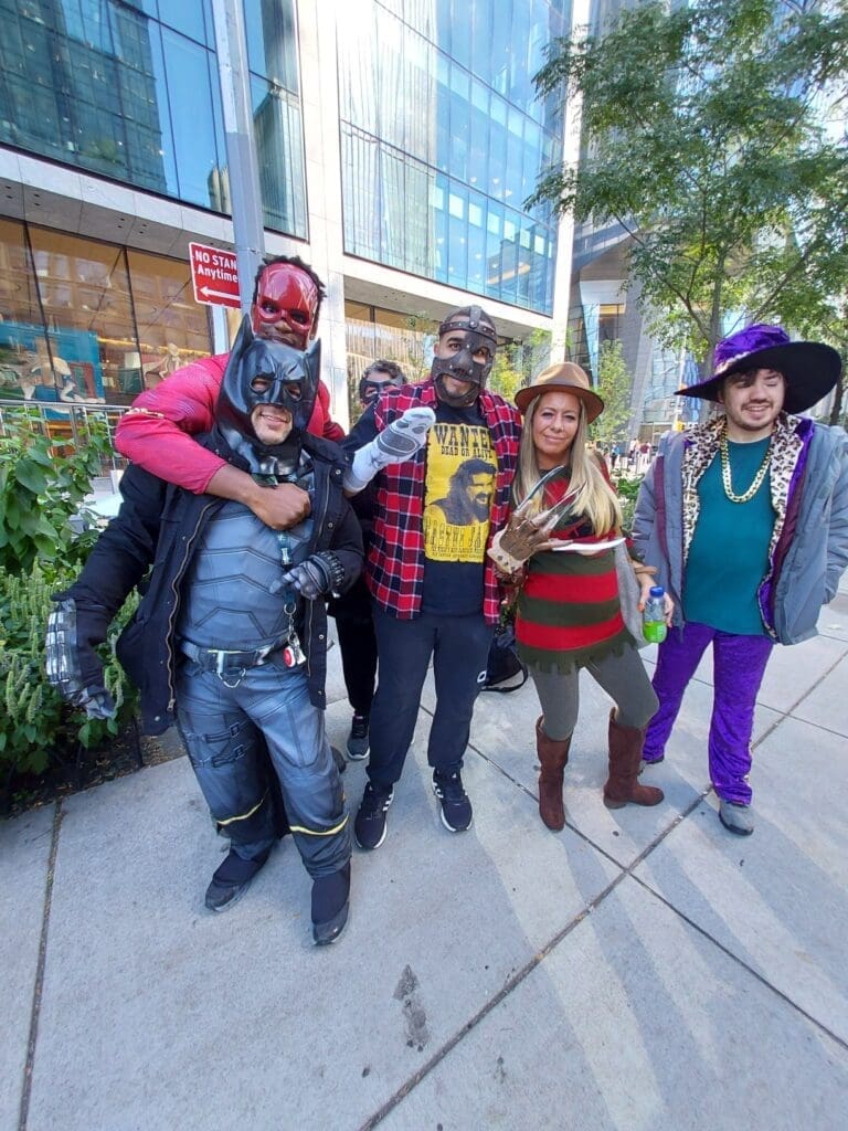 Five people in colorful costumes posing outdoors on a sunny day.