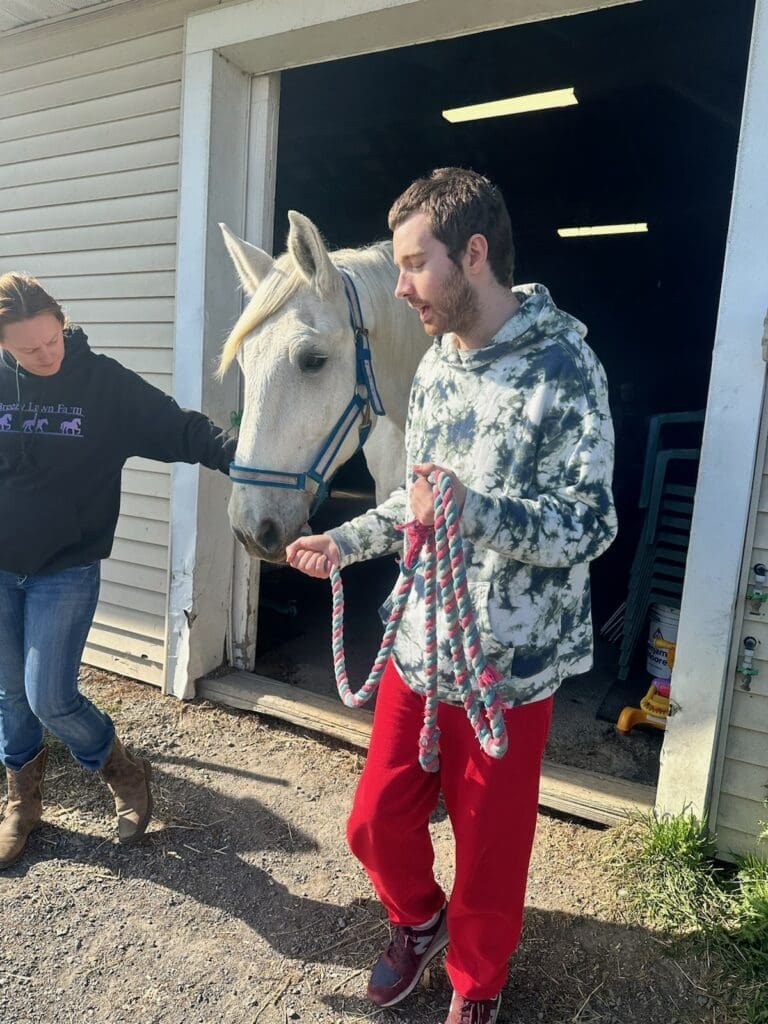 A man holding a white horse by the reins outside a barn.