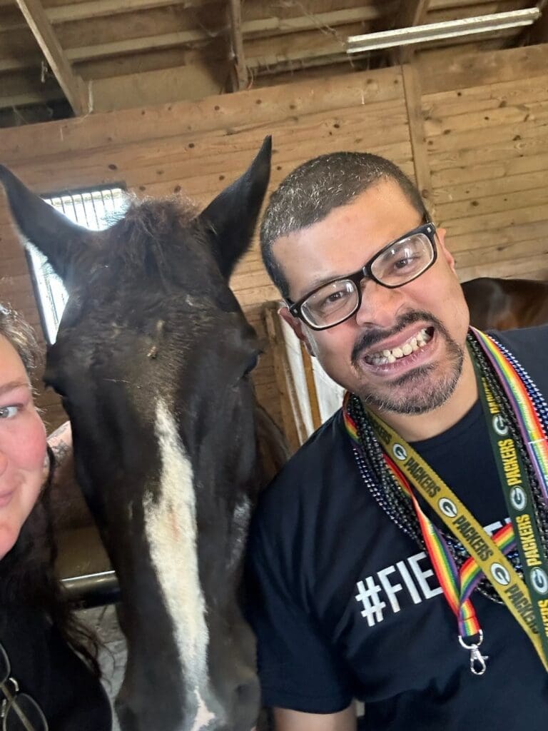 A man holding a white horse by the reins outside a barn.