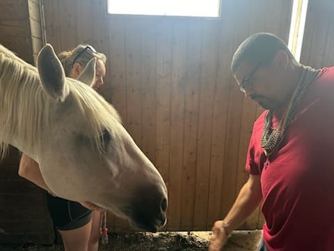 A man holding a white horse by the reins outside a barn.