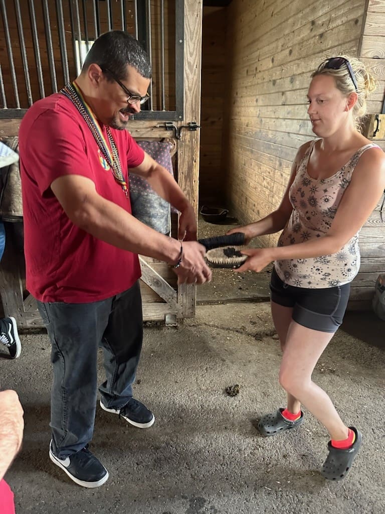 A man holding a white horse by the reins outside a barn.