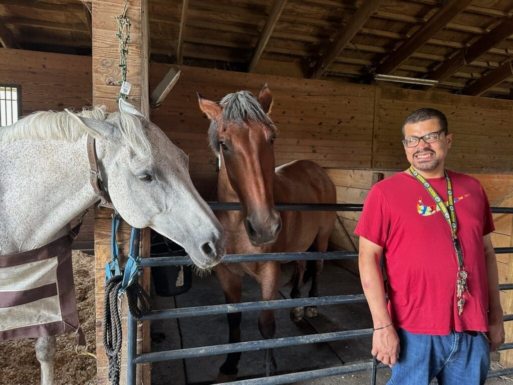 A man holding a white horse by the reins outside a barn.