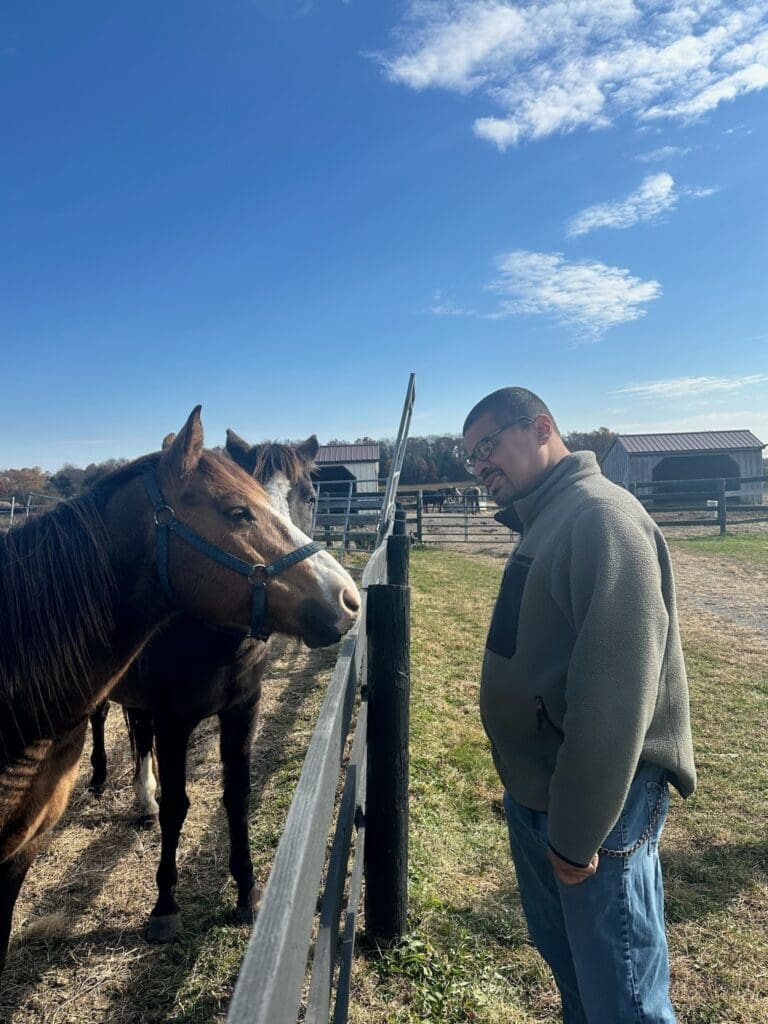 A man holding a white horse by the reins outside a barn.