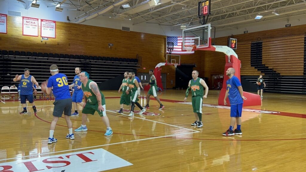 Youth basketball game with players in green and blue uniforms on a gym court.