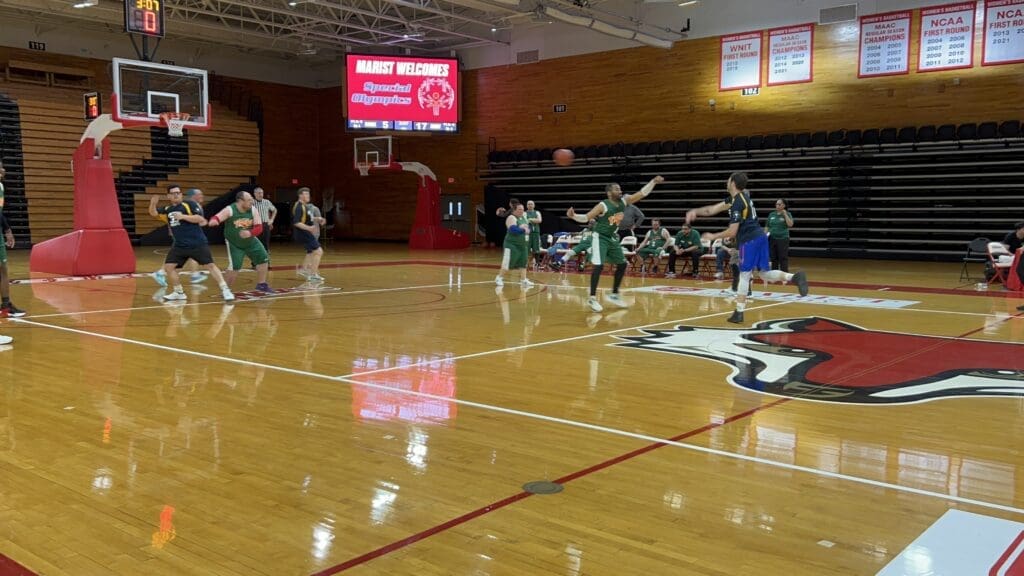 Indoor basketball game with players in green and white uniforms.