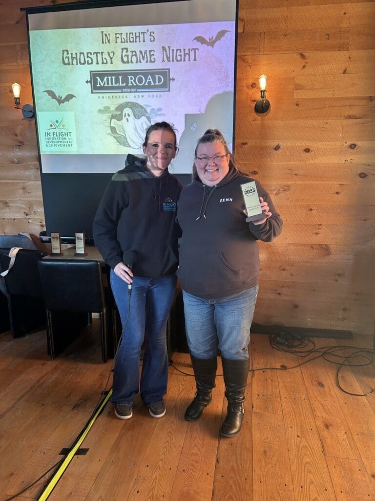 Two women standing together in a cozy wooden room, smiling and holding a book.