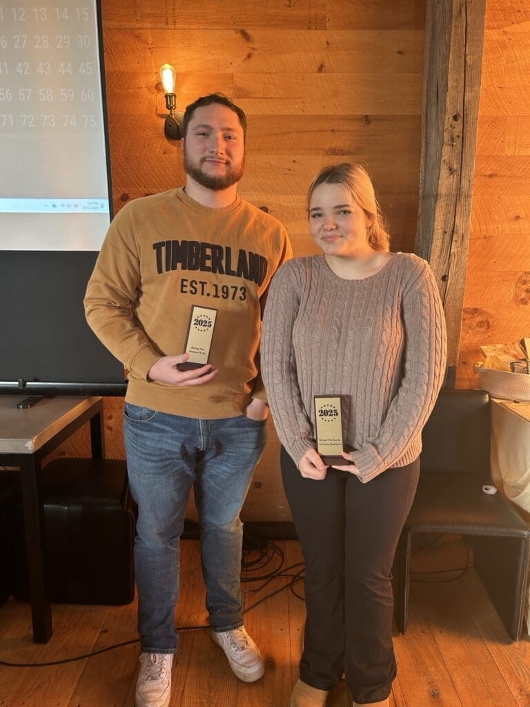Two people holding awards in a cozy wooden room.