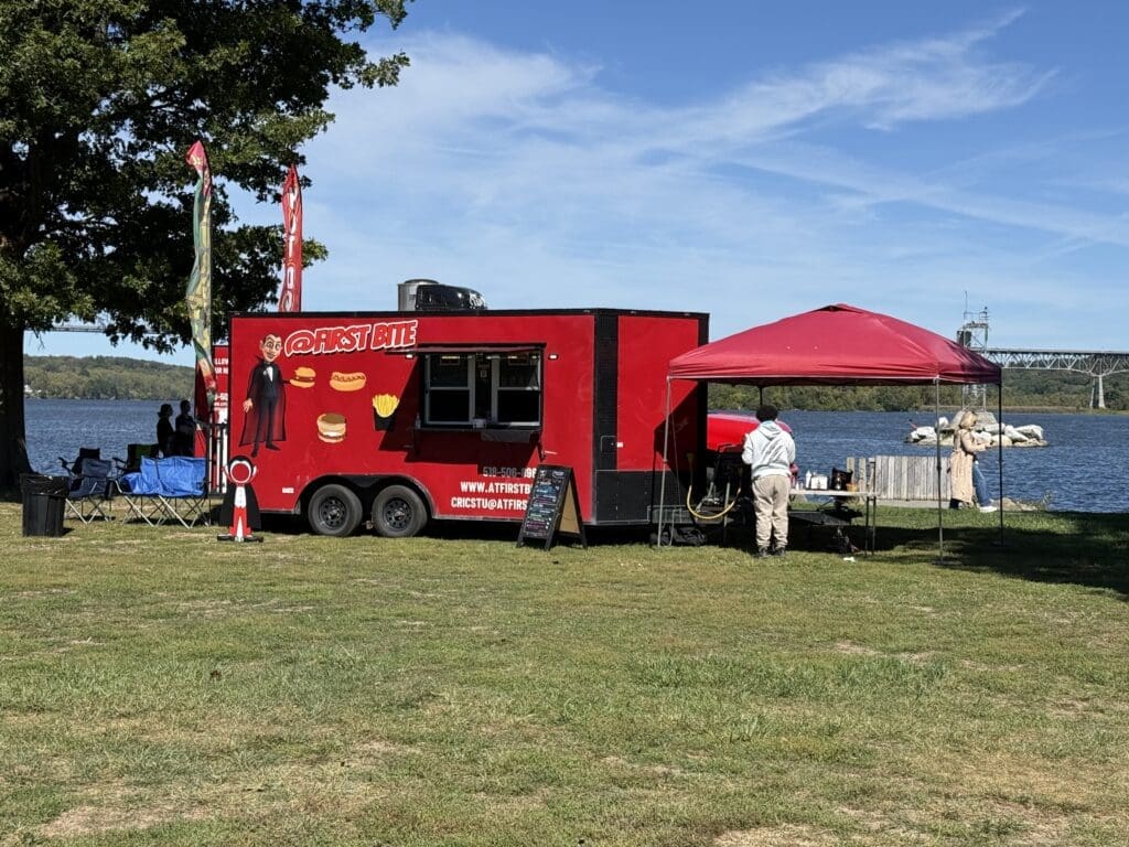 A red food truck and a red canopy set up in a grassy area on a sunny day.
