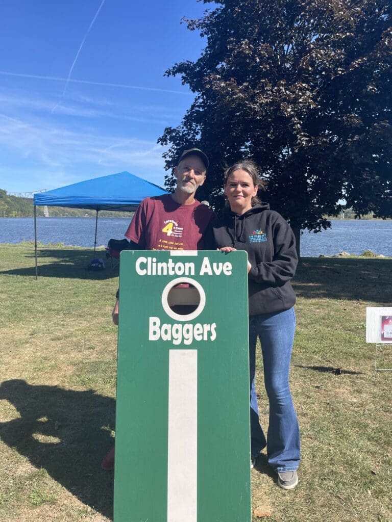 Two people smiling behind a sign that reads 'Clinton Ave Boggers' outdoors.