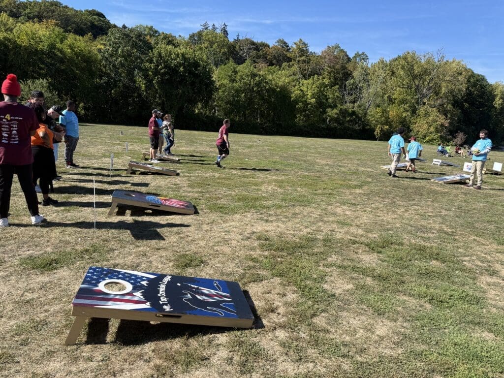 People playing cornhole on a grassy field with trees in the background.