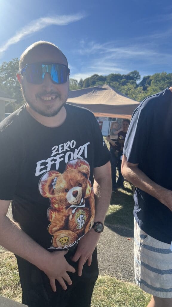 Man wearing sunglasses and a humorous teddy bear 'Zero Effort' t-shirt outdoors.