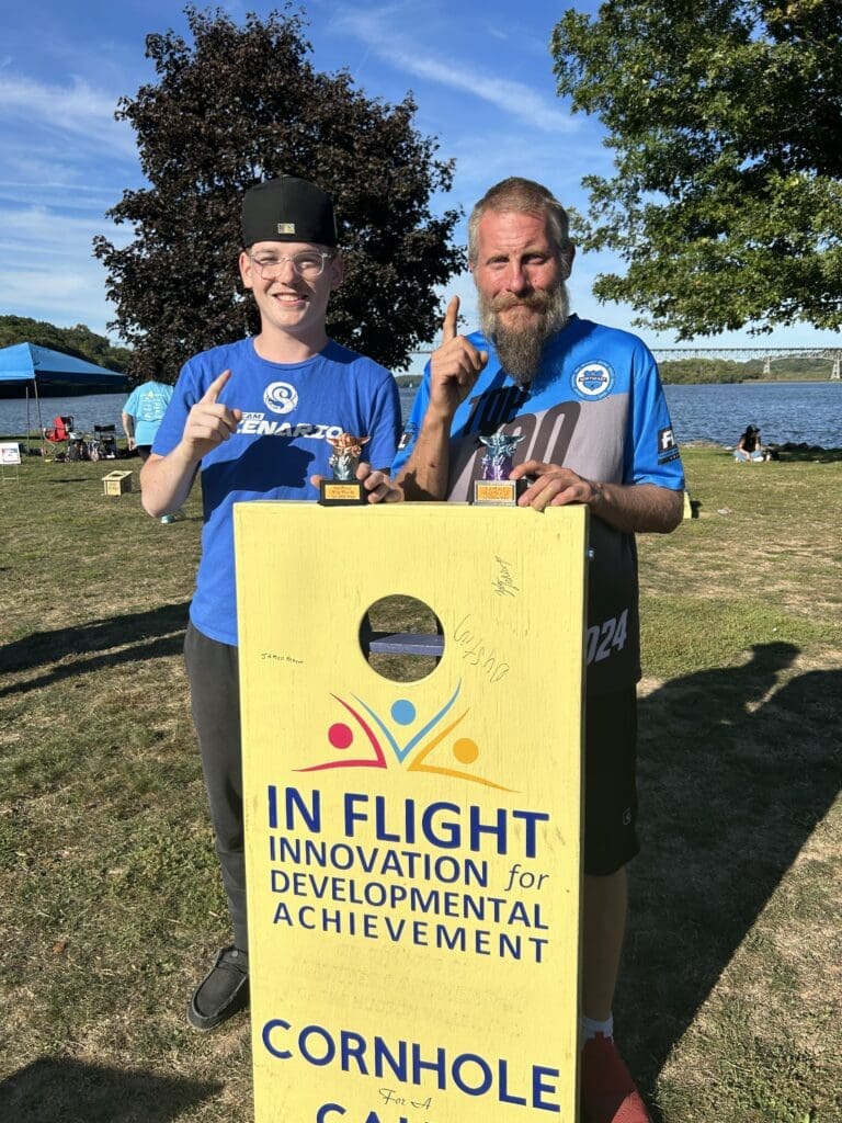 Two people holding a yellow award banner for innovation and development achievement outdoors.