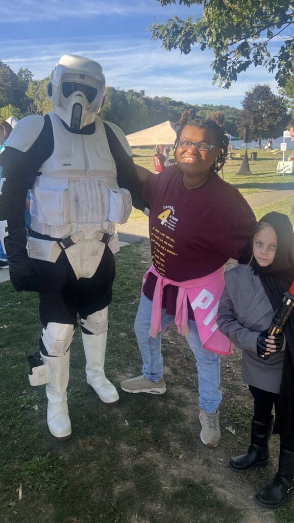 Three people posing outdoors, one in a stormtrooper costume.