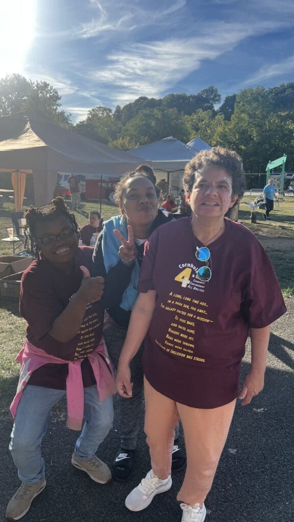 Three women smiling outdoors at a festive event.