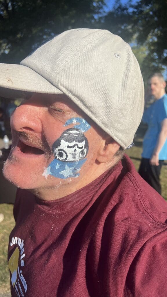Elderly person with a festive face painting of a cartoon-like character.