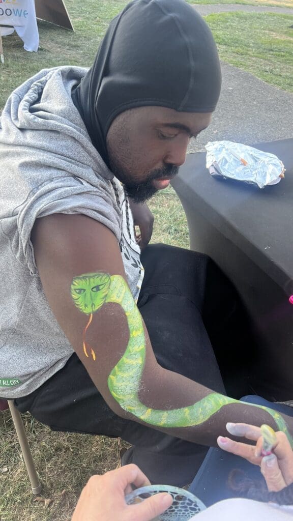 Man with green paint on his arm, sitting at a picnic table outdoors.