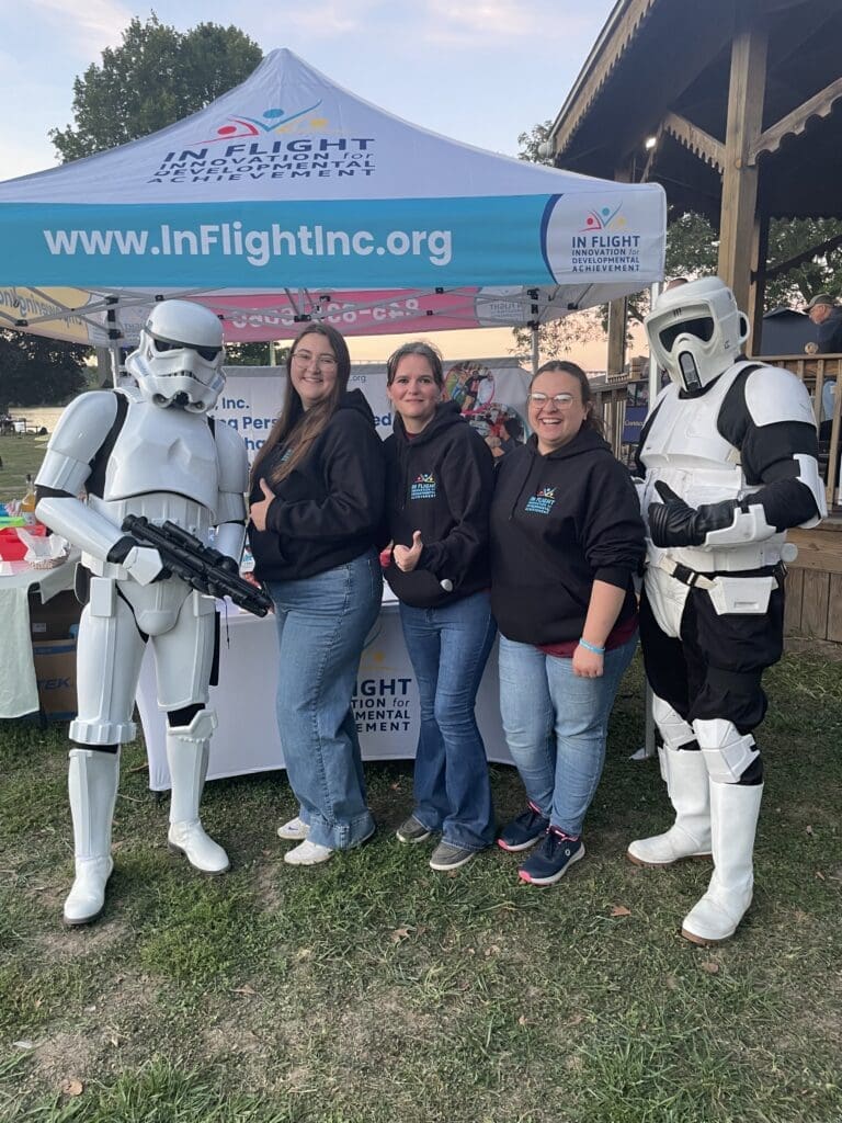 Three people posing with Star Wars stormtroopers at an event booth.