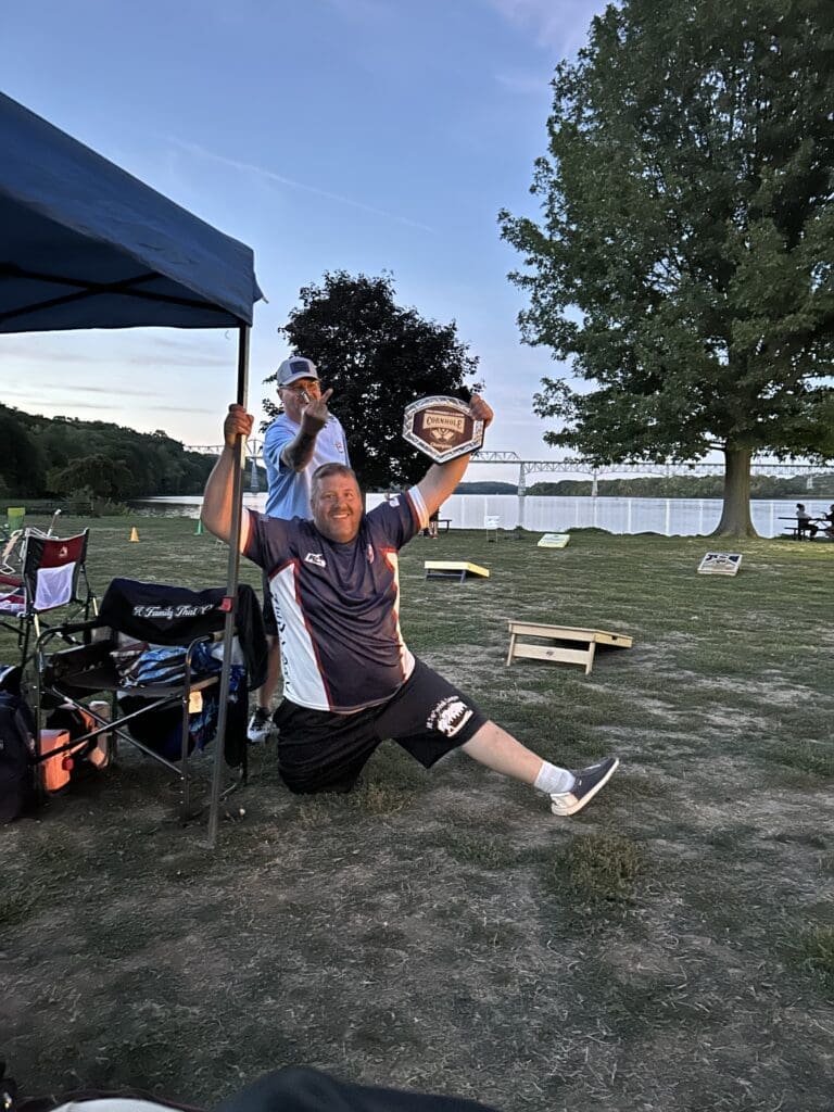 Person jumping joyfully near a lakeside campsite on a sunny day.